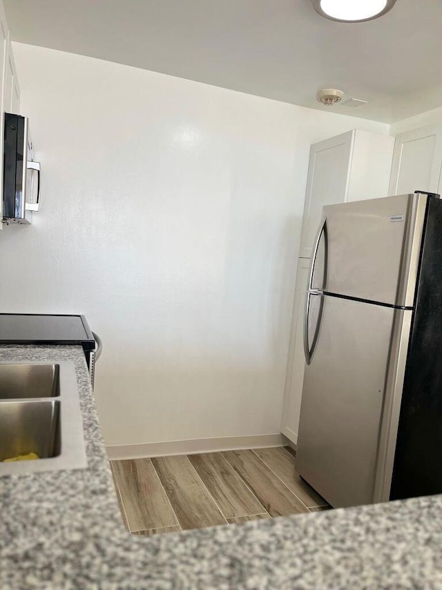 kitchen featuring light wood finished floors, appliances with stainless steel finishes, white cabinetry, and baseboards