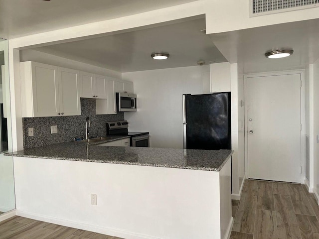 kitchen with visible vents, dark stone counters, a peninsula, stainless steel appliances, and a sink