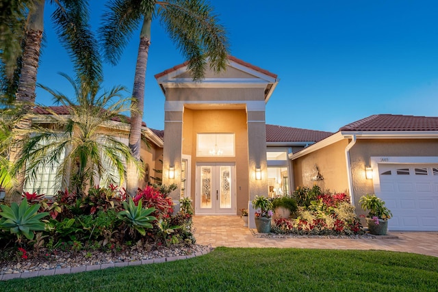 view of front of house with stucco siding, french doors, a front yard, an attached garage, and a tiled roof