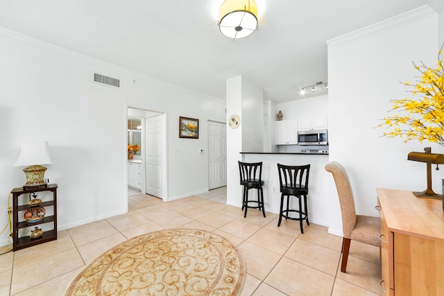 kitchen featuring light tile patterned flooring, visible vents, white cabinetry, ornamental molding, and stainless steel microwave