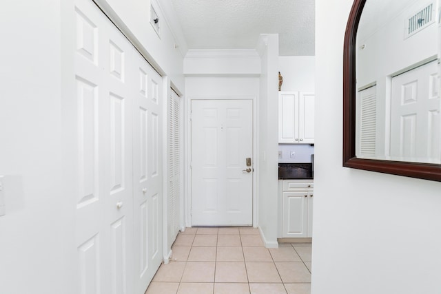 corridor featuring light tile patterned floors, ornamental molding, a textured ceiling, and visible vents