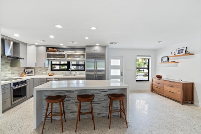 kitchen featuring stainless steel appliances, gray cabinets, visible vents, a sink, and wall chimney exhaust hood