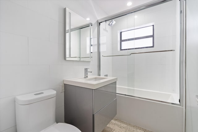 full bathroom featuring toilet, vanity, combined bath / shower with glass door, speckled floor, and tile walls