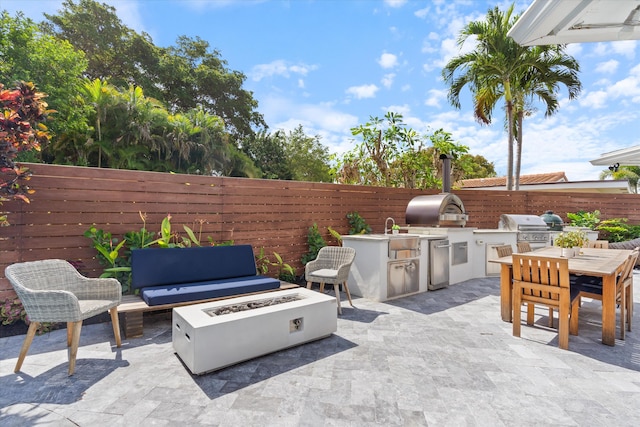 view of patio / terrace featuring area for grilling, outdoor dining space, a sink, fence, and a fire pit