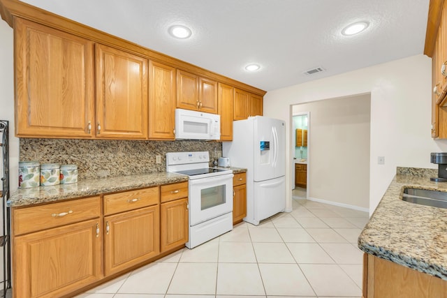 kitchen featuring light stone counters, white appliances, visible vents, brown cabinets, and tasteful backsplash