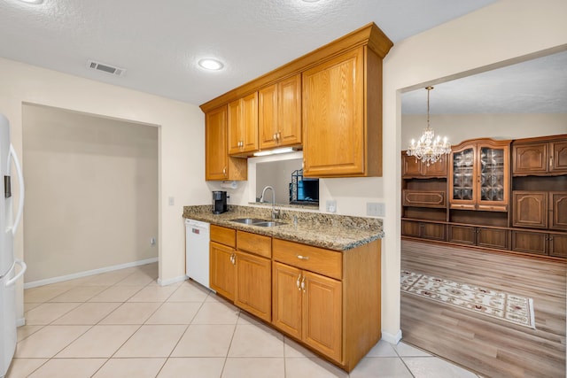 kitchen featuring a notable chandelier, visible vents, white dishwasher, a sink, and light stone countertops