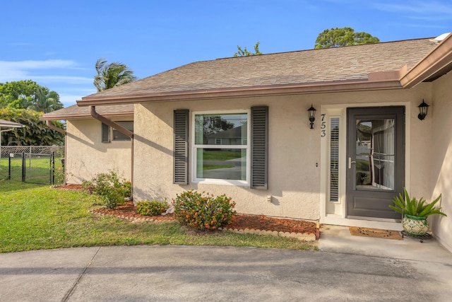 property entrance with a yard, fence, stucco siding, and roof with shingles