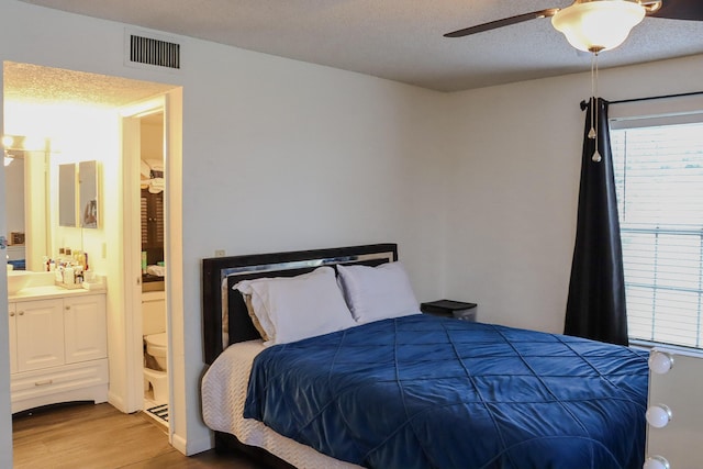 bedroom with visible vents, connected bathroom, wood finished floors, a textured ceiling, and a ceiling fan