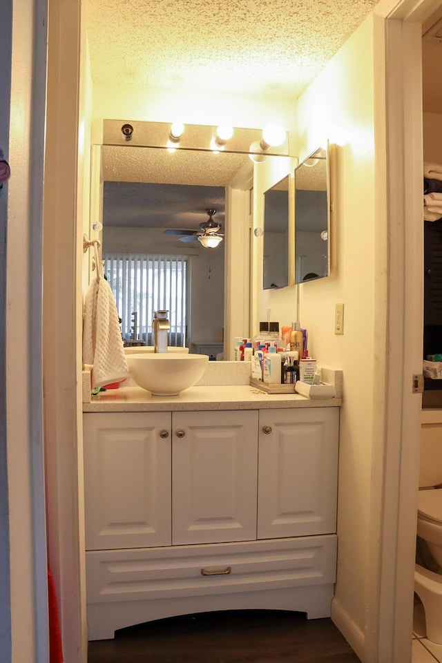 bathroom with vanity, toilet, ceiling fan, and a textured ceiling