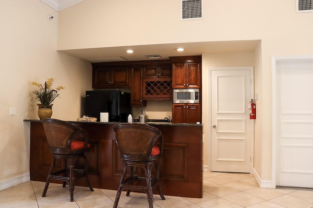 bar with light tile patterned floors, stainless steel microwave, visible vents, and freestanding refrigerator