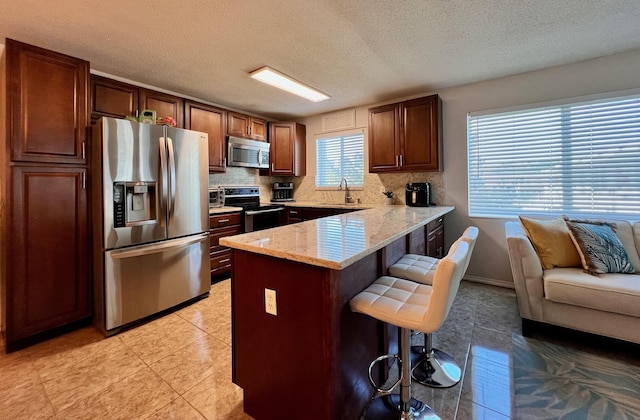 kitchen featuring tasteful backsplash, a breakfast bar area, a peninsula, stainless steel appliances, and a sink