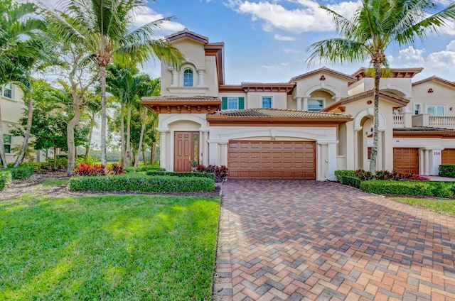 mediterranean / spanish-style home featuring decorative driveway, a tile roof, stucco siding, an attached garage, and a front yard