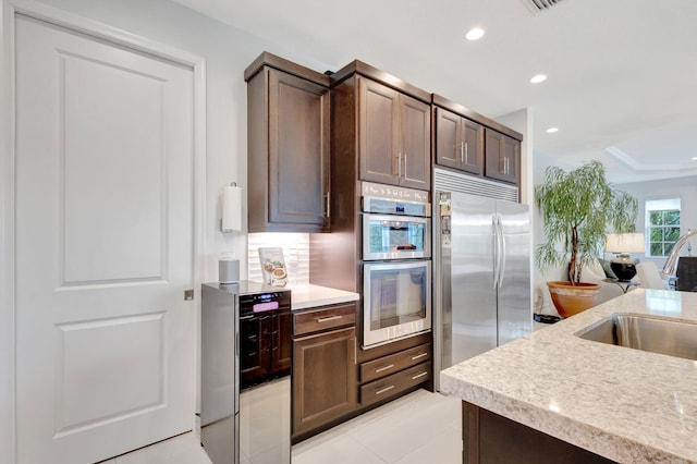 kitchen with appliances with stainless steel finishes, light countertops, dark brown cabinets, a sink, and recessed lighting