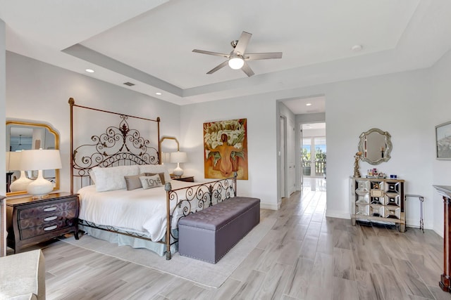 bedroom featuring baseboards, a tray ceiling, a ceiling fan, and light wood-style floors