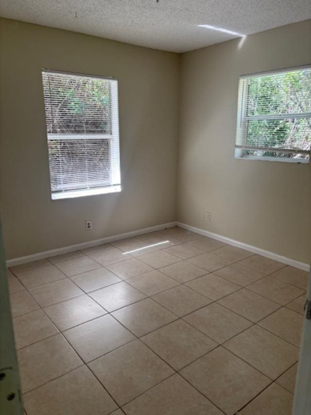 empty room featuring light tile patterned floors, baseboards, and a textured ceiling