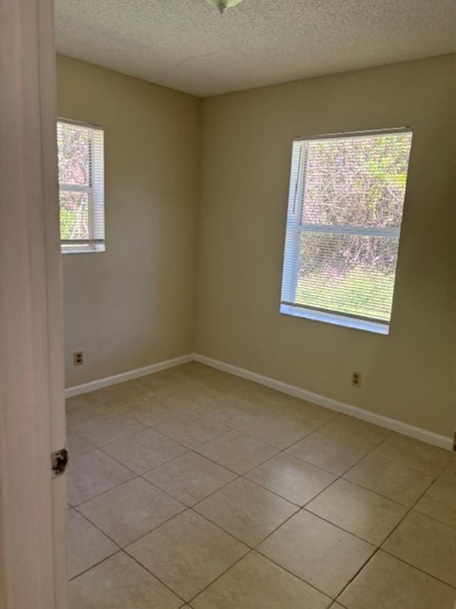 empty room featuring a textured ceiling, baseboards, and light tile patterned floors