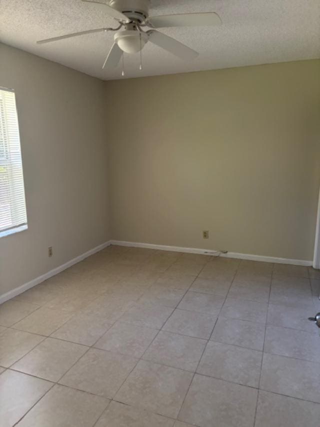 spare room with ceiling fan, baseboards, a textured ceiling, and light tile patterned flooring