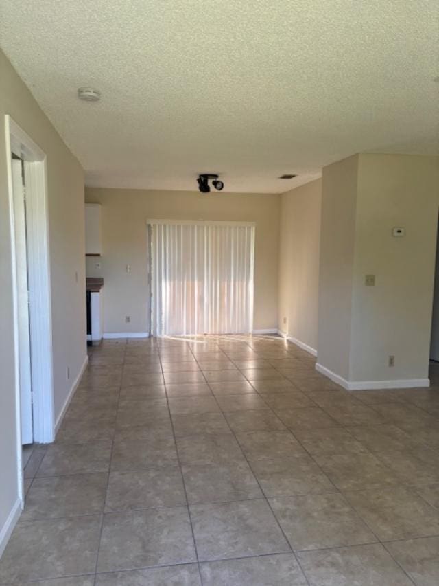 empty room with a textured ceiling, baseboards, and light tile patterned floors