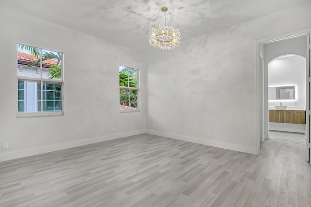 spare room featuring light wood-style floors, baseboards, arched walkways, and an inviting chandelier