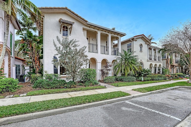 view of front of house featuring a balcony, a tile roof, uncovered parking, and stucco siding