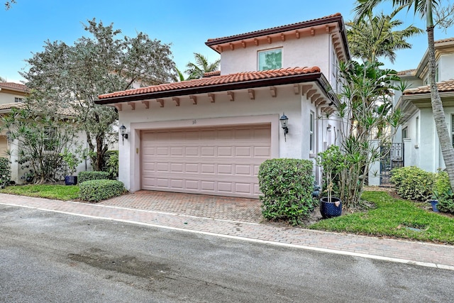 mediterranean / spanish-style home with a garage, a tiled roof, decorative driveway, and stucco siding