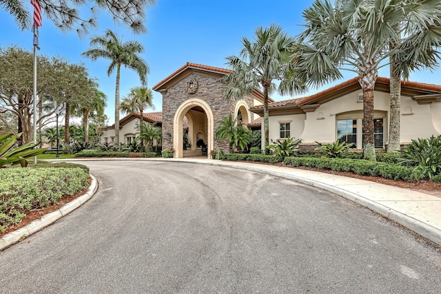 mediterranean / spanish-style home with stone siding, a tile roof, and stucco siding