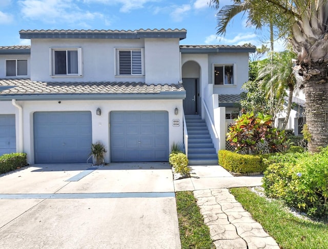 view of front of property with driveway, an attached garage, a tile roof, and stucco siding