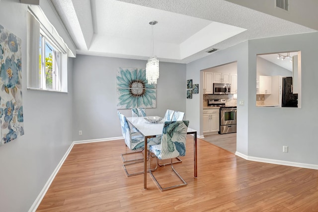 dining space with a tray ceiling, visible vents, a textured ceiling, light wood-type flooring, and baseboards