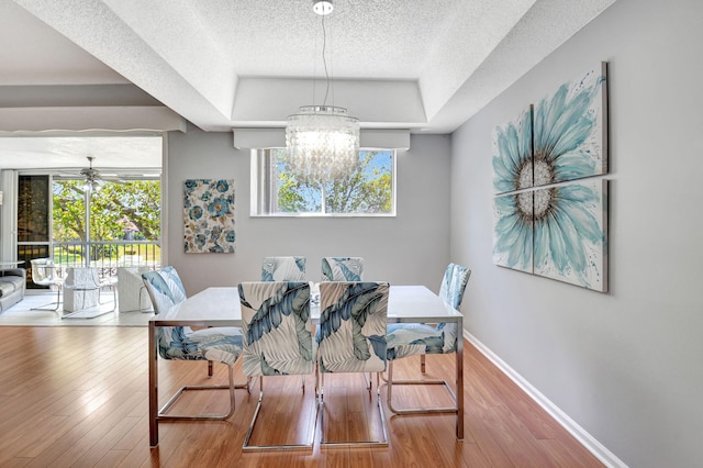 dining area with a textured ceiling, a tray ceiling, wood finished floors, and baseboards