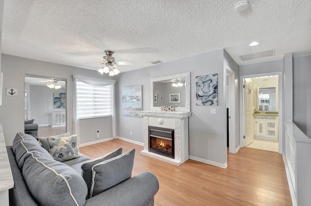 living room featuring a ceiling fan, visible vents, baseboards, light wood-type flooring, and a glass covered fireplace