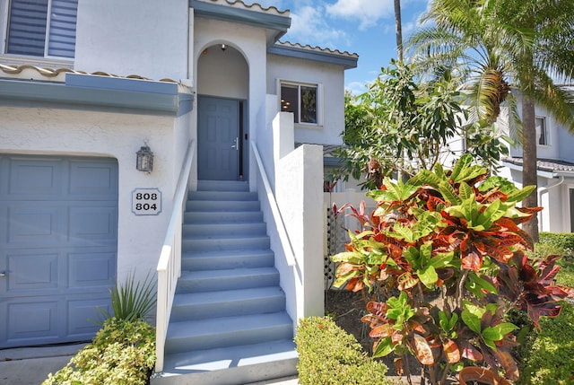 view of exterior entry with a garage, a tiled roof, and stucco siding