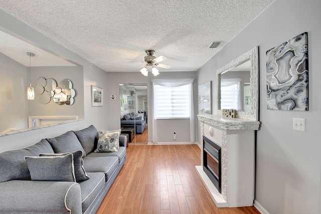 living area featuring light wood finished floors, visible vents, a ceiling fan, a glass covered fireplace, and baseboards