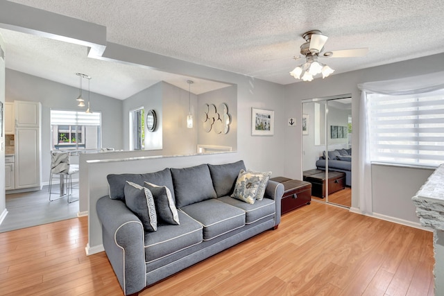 living area with lofted ceiling, light wood-style floors, ceiling fan, a textured ceiling, and baseboards