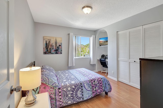 bedroom featuring arched walkways, a textured ceiling, wood finished floors, baseboards, and a closet