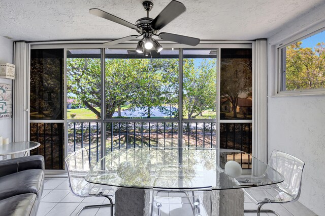 tiled dining space featuring a ceiling fan, a wall of windows, and a textured ceiling