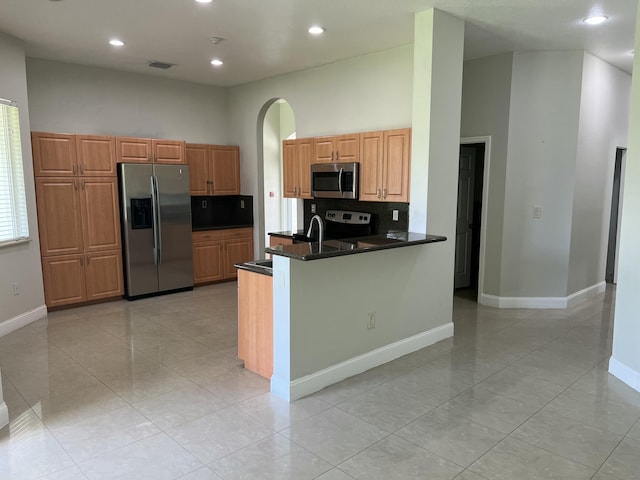 kitchen with a high ceiling, decorative backsplash, appliances with stainless steel finishes, a peninsula, and baseboards