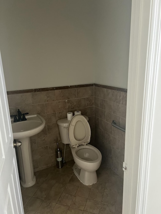 half bathroom featuring toilet, a wainscoted wall, tile patterned flooring, and tile walls