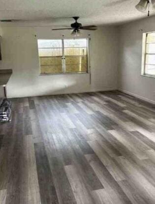 unfurnished living room with dark wood-style flooring, ceiling fan, and a textured ceiling