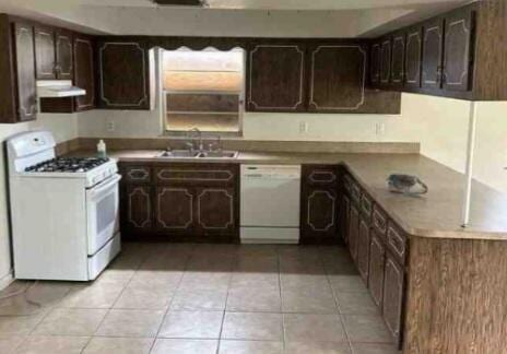 kitchen featuring light tile patterned flooring, under cabinet range hood, white appliances, a sink, and dark brown cabinets