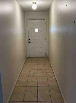 doorway to outside featuring light tile patterned floors, a textured ceiling, and baseboards