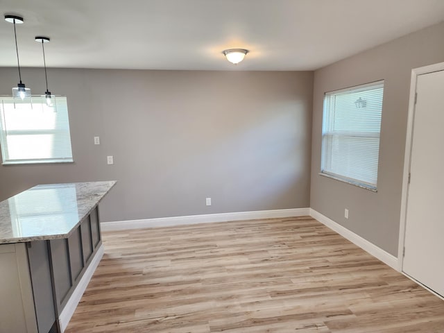 unfurnished dining area featuring light wood-type flooring and baseboards