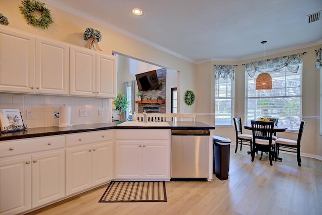 kitchen featuring a peninsula, a sink, stainless steel dishwasher, light wood-type flooring, and crown molding