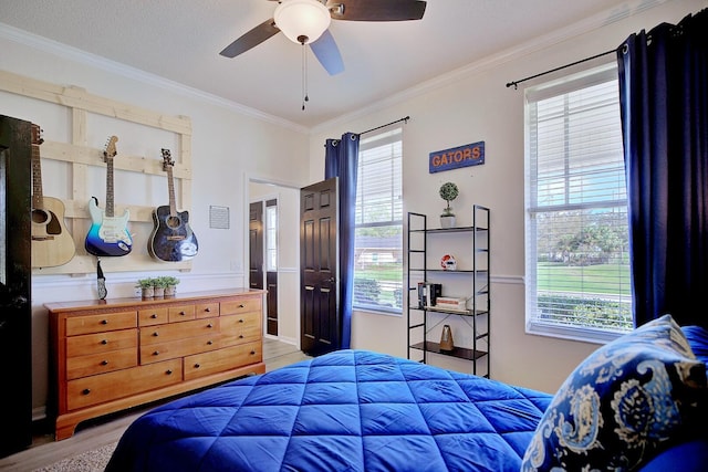 bedroom featuring ornamental molding, multiple windows, light wood-style flooring, and a ceiling fan