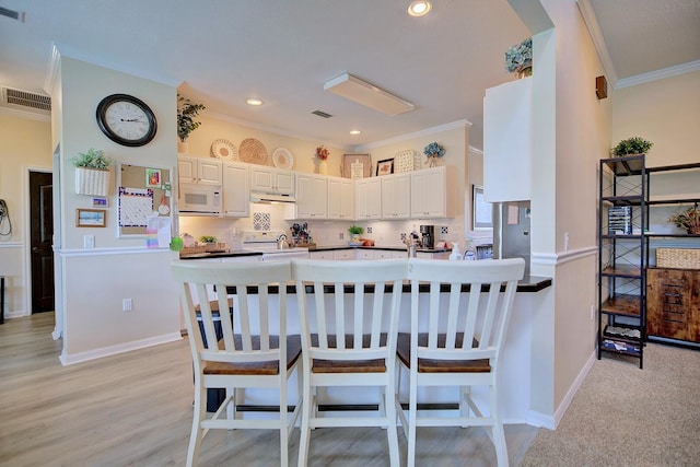 kitchen with white microwave, a peninsula, a breakfast bar, decorative backsplash, and crown molding