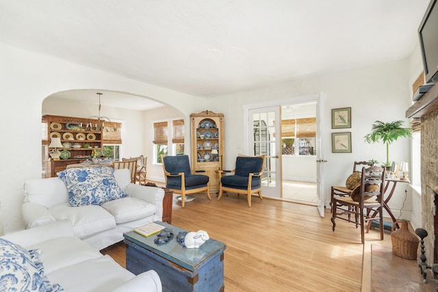 living room with arched walkways, french doors, and light wood-type flooring