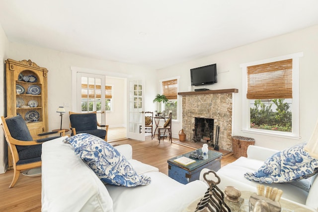 living area featuring a wealth of natural light, french doors, a stone fireplace, and wood finished floors