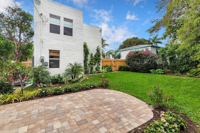 back of house with stucco siding, fence, a lawn, and a patio