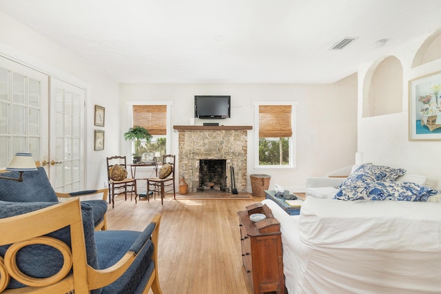 bedroom with a fireplace with raised hearth, multiple windows, wood finished floors, and visible vents