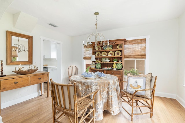 dining space featuring baseboards, light wood finished floors, visible vents, and a notable chandelier