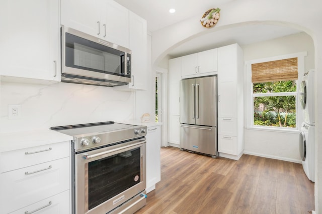 kitchen featuring stainless steel appliances, stacked washer / drying machine, white cabinets, and arched walkways